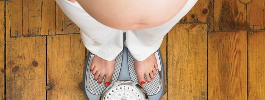 Pregnant woman standing on the weighing machine 